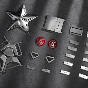 May include: A selection of metallic silver components, including a five-pointed star, rectangular plates, and circular emblems with red and silver accents. The items are arranged on a dark grey surface.