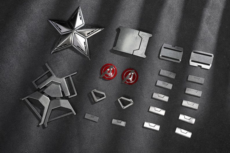 May include: A selection of metallic silver components, including a five-pointed star, rectangular plates, and circular emblems with red and silver accents. The items are arranged on a dark grey surface.