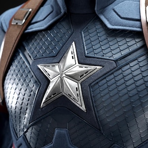 May include: Close-up of a Captain America costume. The navy blue and silver chest piece features a large, silver star emblem. Brown leather straps cross the shoulders. The costume has a textured, scale-like pattern.
