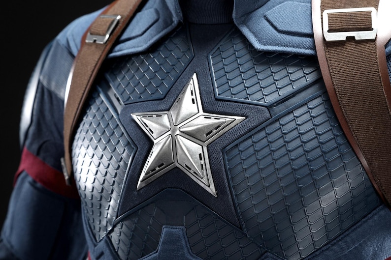May include: Close-up of a Captain America costume. The navy blue and silver chest piece features a large, silver star emblem. Brown leather straps cross the shoulders. The costume has a textured, scale-like pattern.