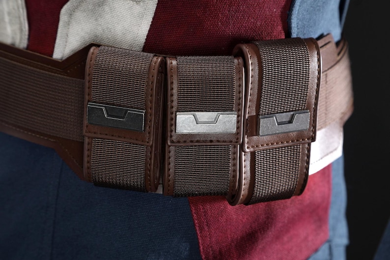May include: A close-up of a brown utility belt with three pouches. The belt is made of a dark brown material with a matching buckle. The pouches have a textured, woven appearance and are secured with metal clasps.