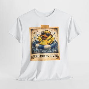 May include: White t-shirt featuring a cartoon duck wearing sunglasses and floating in a blue and white inner tube. The image is framed with a vintage border and the text "ZERO DUCKS GIVEN".