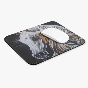 May include: Black rectangular mousepad featuring a detailed illustration of a horse's head. The horse is depicted with a white face, flowing white mane, and brown and gold accents. A white computer mouse rests on the pad.