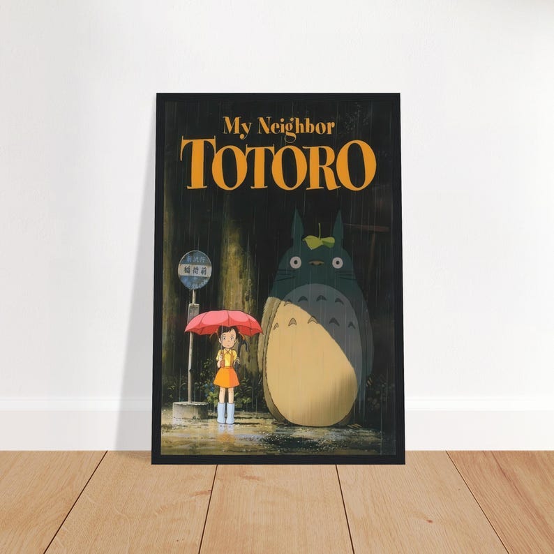 Pode incluir: Um poster emoldurado do filme de anima&ccedil;&atilde;o "Meu Vizinho Totoro". A obra de arte retrata uma menina com um guarda-chuva vermelho, em p&eacute; perto de um ponto de &ocirc;nibus com uma criatura grande e peluda. O t&iacute;tulo "Totoro" est&aacute; em letras grandes e laranja.