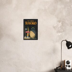 Pode incluir: Um poster emoldurado do filme de anima&ccedil;&atilde;o "Meu Vizinho Totoro". A obra de arte retrata Totoro, um grande esp&iacute;rito da floresta, ao lado de uma menina com um guarda-chuva. O poster tem um fundo escuro com o t&iacute;tulo do filme em letras douradas.