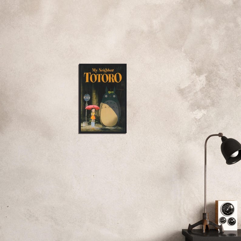 Pode incluir: Um poster emoldurado do filme de anima&ccedil;&atilde;o "Meu Vizinho Totoro". A obra de arte retrata Totoro, um grande esp&iacute;rito da floresta, ao lado de uma menina com um guarda-chuva. O poster tem um fundo escuro com o t&iacute;tulo do filme em letras douradas.