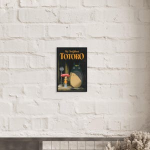 Pode incluir: Um poster emoldurado com o filme de anima&ccedil;&atilde;o "Meu Vizinho Totoro". A obra de arte retrata uma menina com um guarda-chuva vermelho em um ponto de &ocirc;nibus com Totoro. O t&iacute;tulo est&aacute; em letras laranja sobre um fundo preto.