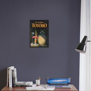Pode incluir: Um poster emoldurado do filme de anima&ccedil;&atilde;o "Meu Vizinho Totoro". A obra de arte retrata Totoro, um grande esp&iacute;rito da floresta, em p&eacute; ao lado de uma menina com um guarda-chuva vermelho em um ponto de &ocirc;nibus. O p&ocirc;ster tem uma moldura preta.