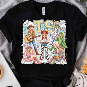 K&ouml;nnte beinhalten: Ein schwarzes Kurzarm-T-Shirt mit einem Grafikdruck von sechs illustrierten Figuren in verschiedenen Outfits, darunter eine Cowgirl mit Gitarre, ein Weltraum-Ranger und ein Dinosaurierkost&uuml;m, mit den gro&szlig;en gelben Buchstaben TS oben.