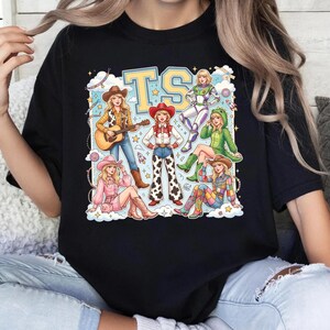 K&ouml;nnte beinhalten: Ein schwarzes T-Shirt mit einem Grafikdruck von sechs illustrierten Figuren in verschiedenen Outfits, darunter ein Cowgirl mit Gitarre, ein Raumanzug und ein Dinosaurierkost&uuml;m, unter den gro&szlig;en gelben Buchstaben TS, umgeben von Wolken und Sternen.