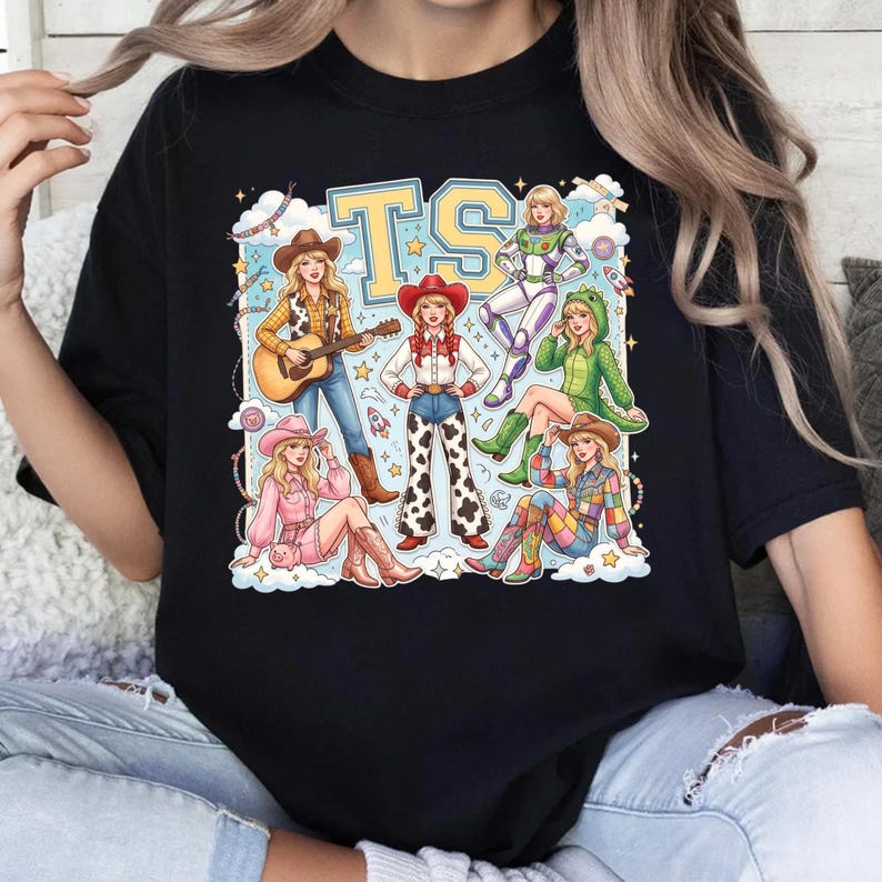 K&ouml;nnte beinhalten: Ein schwarzes T-Shirt mit einem Grafikdruck von sechs illustrierten Figuren in verschiedenen Outfits, darunter ein Cowgirl mit Gitarre, ein Raumanzug und ein Dinosaurierkost&uuml;m, unter den gro&szlig;en gelben Buchstaben TS, umgeben von Wolken und Sternen.