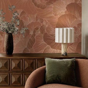 May include: A room interior featuring terracotta wallpaper with a white line-drawn floral pattern, a dark wood sideboard, a tall dark vase with dried branches, a white pleated lamp on a marble base, and a textured rust-coloured sofa with a green pillow.