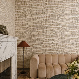 May include: A stylish living room with a beige sofa, marble fireplace, and a dark brown floor lamp. The walls are adorned with textured, off-white wallpaper. A round, dark green table and flowers add to the room's decor.