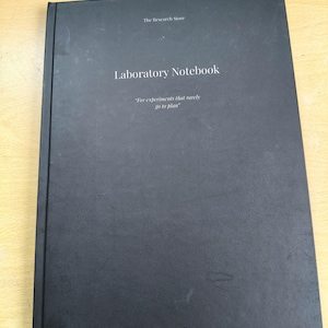 May include: A black Laboratory Notebook with the text "The Research Store" at the top and "Laboratory Notebook" in the centre. The notebook includes the quote "For experiments that rarely go to plan" and "Undated Editon" at the bottom.