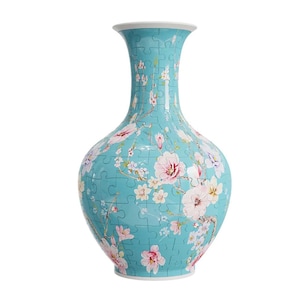 Puede incluir: Un jarrón turquesa con un diseño floral. El jarrón presenta flores rosas y blancas con hojas verdes. El diseño está hecho de piezas de rompecabezas. Un objeto decorativo.