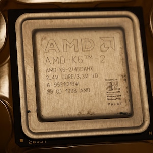 May include: Close-up of an AMD-K6 processor. The silver-colored CPU has the text "AMD-K6 TM-2" and other technical specifications printed on its surface. The processor is designed for Microsoft Windows NT and Windows 95.