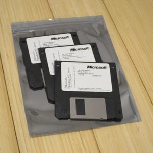 May include: Three black 3.5-inch floppy disks with white labels, featuring the Microsoft logo and text. The disks are labeled "Microsoft Windows NT Server" and are packaged in a clear plastic bag. The disks are on a wooden surface.
