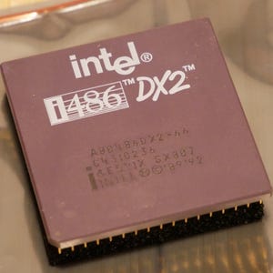 May include: A close-up of a vintage Intel i486 DX2 processor. The processor is a rectangular shape with a dark purple top and gold pins along the bottom edge. The Intel logo and "i486 DX2" are printed in white.