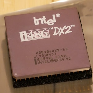 May include: A close-up of a vintage Intel i486 DX2 processor. The processor has a purple top with white text that reads "intel", "i486 DX2", and other model information. The bottom has gold pins.