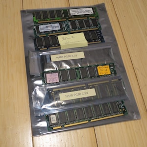 May include: Several computer memory modules are visible inside clear plastic packaging. The modules have green circuit boards with black chips and gold connectors. Some modules have labels indicating memory size and specifications, such as "16MB PC66 3.3V" and "32MB PC66 3.3V".