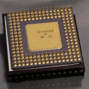 May include: Close-up of a square computer processor with numerous gold pins. The central square has the text "52340833CA A4 BH 51" printed on it. The processor is dark gray and gold in color.