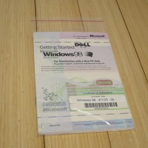 May include: A sealed Microsoft Windows 98 Second Edition software package. The package includes a "Getting Started" guide and a "Certificate of Authenticity" label with a product key and barcode. The package is in a clear plastic bag.