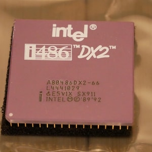 May include: A vintage Intel i486 DX2 processor. The processor has a purple top with white text that reads "intel i486 DX2". Additional text includes model numbers and the Intel logo. The bottom edge has gold pins.