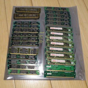 May include: A collection of computer RAM modules, featuring green circuit boards with various chips and labels. Some modules are tan, while others are green. The modules are arranged in rows and columns, with some in a clear plastic bag.