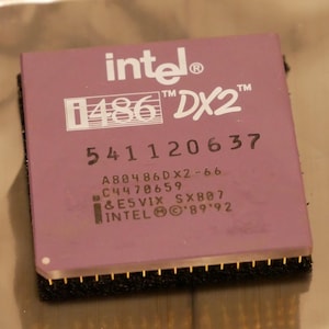 May include: A close-up of an Intel i486 DX2 processor. The processor has a mauve top with white text that reads "intel i486 DX2". The bottom edge has gold pins. The processor is a vintage computer component.