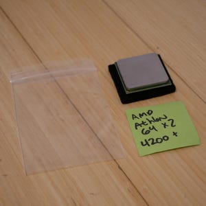 May include: A computer processor, likely an AMD Athlon 64 X2 4200+, sits on a black pad. A clear plastic bag is to the left. A green sticky note displays the processor's specifications.
