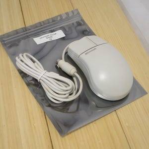May include: A white Microsoft mouse with a cord, resting on a gray plastic bag. The mouse has two buttons and a scroll wheel. The cord is coiled neatly. A label on the bag reads "Microsoft mouse 6/9/25 02".