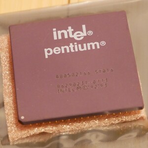 May include: A close-up of a vintage Intel Pentium processor. The processor is a rectangular shape with a mauve-colored top. The Intel and Pentium brand names are printed in white. The processor has gold pins on the bottom.