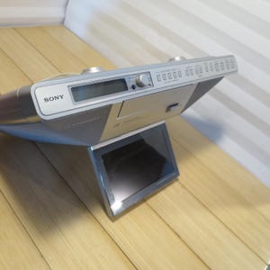 May include: Silver Sony CD player with a built-in screen. The player has a digital display, a CD tray, and several buttons. The unit is angled on a stand, and the Sony logo is visible on the front.