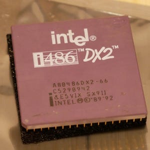 May include: A close-up of a vintage Intel i486 DX2 processor. The processor has a purple top with white text that reads "intel i486 DX2". The bottom edge has gold pins. The processor is on a black foam base.