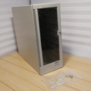 May include: A silver-colored server rack cabinet with a glass door and a lock. The cabinet has a series of vertical vents on the side. A small bag with several clear plastic pieces and a key is in front of the cabinet.