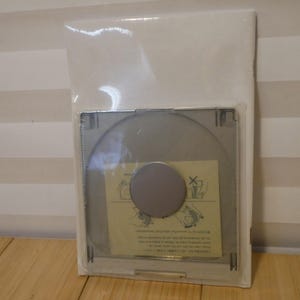May include: A clear plastic package containing a silver-colored, circular object with a gray center. A small, rectangular paper with illustrations and text is visible. The package is sealed and appears new.