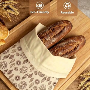 May include: A cream-colored fabric bread bag featuring a repeating brown pattern of various leaves and circular floral shapes. Two crusty brown loaves of bread are tucked inside the open bag, which is labeled with Eco-Friendly and Reusable text.