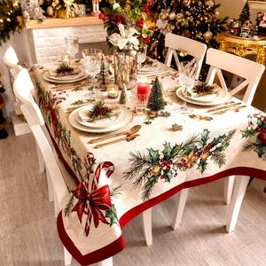 May include: A rectangular tablecloth featuring a festive print of holly leaves, red berries, pine branches, and candy canes with red bows. The fabric has a cream-colored base with a solid red border, covering a dining table set with white plates.