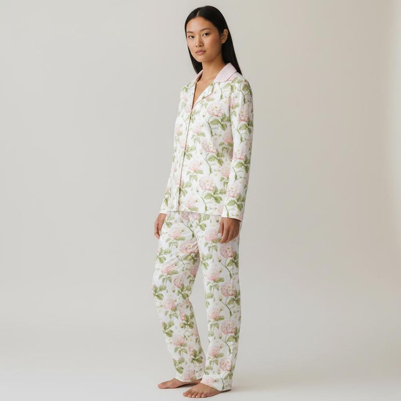 May include: A two-piece pajama set featuring a floral pattern of pink roses and green leaves on a white background. The long-sleeved top has a pink collar, and the pants are straight-legged. The pajamas are made of a soft, lightweight fabric.