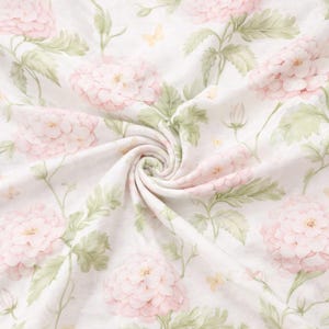 May include: A white fabric with a repeating floral pattern. Large, soft pink flowers with yellow centers are interspersed with green leaves and small yellow butterflies. The fabric is gathered in a swirl.