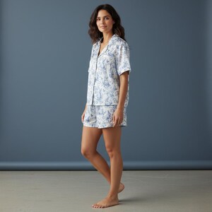Op de afbeelding: Een tweedelige pyjamaset met een wit en blauw bloemenpatroon. De set bestaat uit een overhemd met korte mouwen en bijpassende shorts. De stof lijkt licht en comfortabel, geschikt voor nachtkleding.