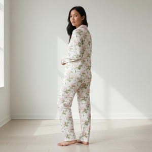 May include: A matching pajama set featuring a floral pattern of pink roses and green leaves on a white background. The set includes a button-down top with a pink collar and long pants. The pajamas are made of a soft, comfortable material.