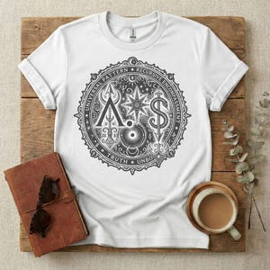 Pode incluir: Uma t-shirt branca de manga curta com uma grande impressão gráfica circular preta no peito. O design inclui uma estrela central, uma cobra, uma seta e vários símbolos, rodeados pelo texto "UNIVERSAL PATTERN RECURSIVE ENCOMPASSMENT TRUTH UNBOUND".