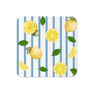 May include: A square coaster featuring a white background with vertical blue stripes. The surface is decorated with a repeating pattern of whole yellow lemons, sliced lemon segments, and small green leaves scattered across the striped design.