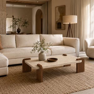 May include: A neutral-toned living room with a large sectional sofa, a coffee table, and a round armchair. The coffee table has a light-colored top and dark wooden legs. A jute rug covers the floor, and a floor lamp stands nearby.