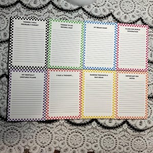 May include: A set of eight notepads with lined pages and colorful checkered borders. Each notepad has a different title, including "Things I Will Probably Forget" and "Plans for World Domination."