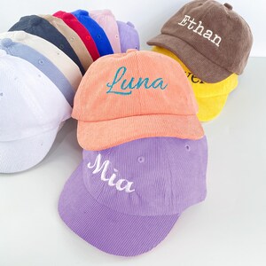 Peut inclure: Plusieurs casquettes de baseball en velours côtelé de différentes couleurs, dont blanc, marine, beige, rouge, bleu, rose et violet. Certaines casquettes sont brodées de noms tels que "Luna", "Mia" et "Ethan".