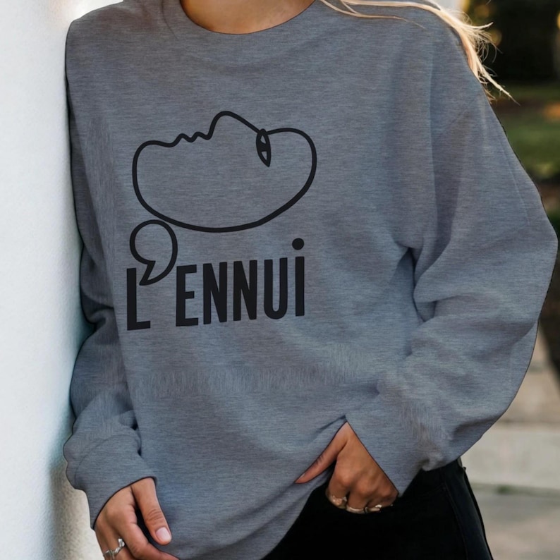 May include: A gray sweatshirt with the word "L'ENNUl" in black, along with a black line drawing of a face. The sweatshirt is a casual style, suitable for everyday wear.