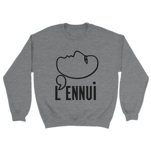 Peut inclure: Un sweat-shirt gris chiné avec un dessin au trait noir minimaliste d'un visage et le mot "L'ENNUl" en noir, un mot français signifiant ennui. Le design est centré sur le devant du vêtement à manches longues.