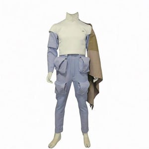 May include: A white mock-neck top paired with light blue cargo pants featuring four large pockets. A tan and brown patterned shawl drapes over the left shoulder. The ensemble is displayed on a mannequin, showcasing a structured design with utility-style elements and a clean, layered silhouette.